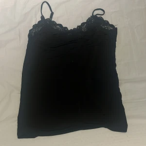Svart spetslinnetopp från Object - Säljer en svart linnetopp från Object med tunna axelband och vacker spetsdetalj upptill. Toppen har en stilren och enkel design som känns både trendig och tidlös. 