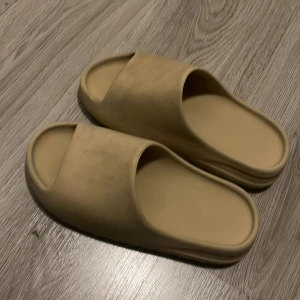 Adidas Yeezy Slides - Mysiga tofflor i stilren design Perfekta för både hemmamys och snabba ärenden till brevlådan. I en varm beige ton som passar med allt och ger en clean look. Gjorda i mjukt, formande material för maximal komfort. Storlek 42