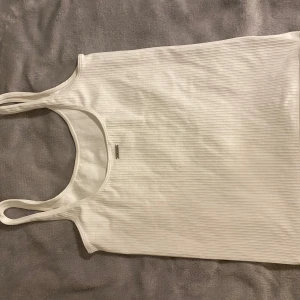 Vit ribbad linnetopp - Säljer en stilren vit ribbad linnetopp med smala axelband. Den passar till en vanlig outfit men oxå till träning eller gym, aldrig använt men provat en gång och väldigt bra matrial 