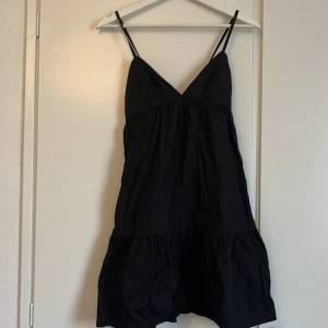 Svart kort klänning med snörning - Säljer en svart kort klänning med tunna axelband och v-ringad front. Klänningen har en volang nedtill och snörning i ryggen som ger en snygg detalj. Perfekt för dig som gillar en enkel men stilren look. Materialet känns lätt och luftigt.