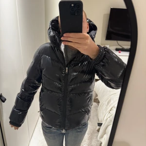 Svart glansig pufferjacka från Colmar - Säljer en svart, glansig pufferjacka från Colmar!! Supersnygg att ha på vintern, jag har bara använt den en vinter, väldigt sparsamt så att den har inga hål eller liknande. Det finns minimala täcken på användning precis upptill luvan där den är lite ljusare pga smink. Annars är den i princip i nyskick. Säljer då jag vill köpa en annan vinterjacka. Storlek är 16 år men skulle säga att det är samma size som XS💗