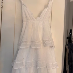 Vit volangklänning från Gina Tricot - Supersöt vit kortklänning från Gina Tricot med tunna axelband, v-ringning och flera lager volanger. är tyvärr för liten och kommer inte till användning. Aldrig använd