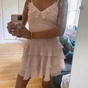 Ljusrosa volangklänning med smala axelband - Supersöt ljusrosa kortklänning med flera lager volanger och smala axelband. Klänningen har v-ringad hals och ärmlös design, perfekt för sommarens alla tillfällen. Materialet är lätt och luftigt, vilket gör den extra bekväm och flowy. Slutsåld!