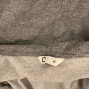 Grå hoodie med dragkedja från Cubus  - Mysig grå hoodie med huva och hel dragkedja framtill från Cubus . Tröjan har långa ärmar, ribbade muddar och två fickor på magen. Perfekt för chill dagar och enkel att matcha med jeans eller leggings.