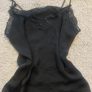 Svart spetlinne   - Supersnyggt svart linne från Rut&Circle med tunna axelband och spetsdetaljer. Perfekt för dig som gillar stilrena och trendiga plagg. Storleken är s men kan passa m också.