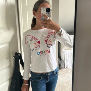 Vit långärmad Kenzo tröja med tryck - Vit långärmad tröja från Kenzo med färgglatt tryck av två tigrar och logga på bröstet. Tröjan har rund halsringning och är i mjuk bomull, perfekt för dig som gillar statement-plagg med cool design.