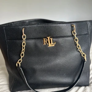 Svart axelväska från Ralph Lauren - Stilren svart axelväska från Ralph Lauren med guldfärgade kedjedetaljer och RLL-logga framtill. 