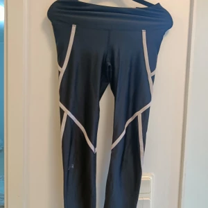 Svarta träningstights med vita detaljer - Snygga svarta träningstights med vita linjer längs benen som ger en sportig look. Hög midja och stretchigt material som sitter skönt och följer kroppen perfekt under träningen.