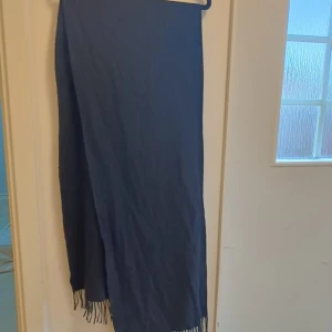 Svart halsduk med fransar - En stilren svart halsduk med klassiska fransar i ändarna. Perfekt att slänga över axlarna för en enkel men snygg look. Halsduken är lång och passar bra att vira flera varv runt halsen.