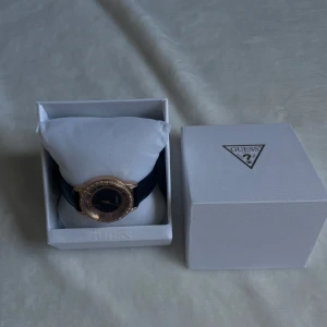 Rosefärgad Guess klocka med svart band  - Rosefärgad Guess-klocka med svart band. Glittrig urtavla med diamanter runt. Nästan ny, bara använd några gånger! (fortfarande garanti)