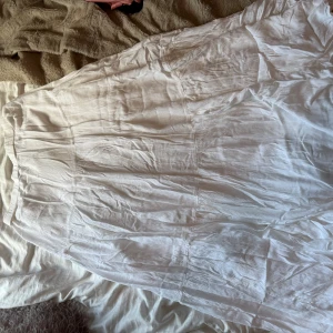 Vit långkjol från Stradivarius - Supersnygg vit långkjol från Stradivarius i mjukt och luftigt bomullstyg. Kjolen har en elastisk midja och flera volanger som ger en flowy och chill vibe. Perfekt för varma dagar och enkel att styla med crop tops eller sneakers.