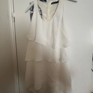 Vit ärmlös klänning med dragkedja - Säljer en stilren vit ärmlös klänning med lager-på-lager design. Klänningen har en dragkedja i ryggen och en luftig passform. Perfekt för sommarens alla tillfällen!