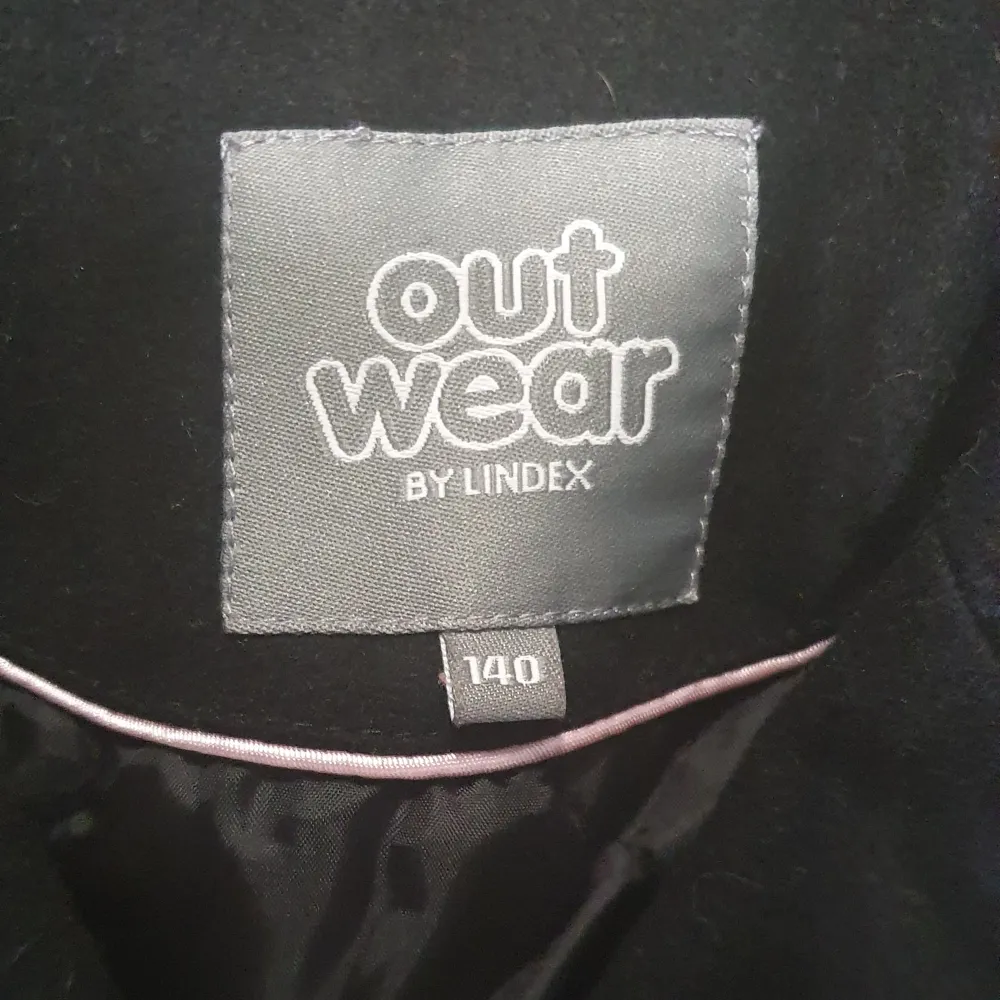 Snygg svart kappa från Lindex med dubbelknäppning och klassisk krage. Perfekt för kyligare dagar med sin stilrena design och praktiska knappar. Ett måste i garderoben för en elegant look.. Takit.