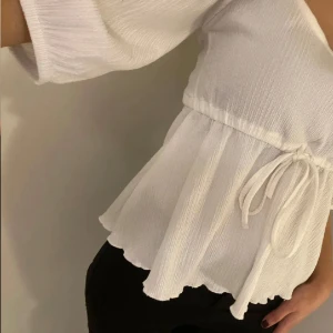 Vit blus - Säljer en söt vit blus med knytband i midjan och volangdetaljer. Blusen har trekvartsärmar och en luftig passform, perfekt för vår och sommar.