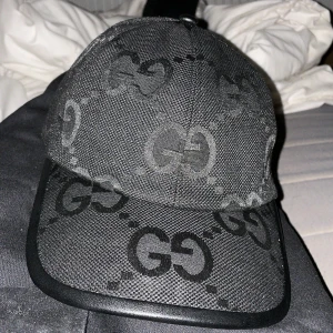 Gucci jumbo keps - Snygg svart keps från Gucci med det ikoniska GG-monogrammet i svart. Kepsen har en justerbar rem baktill för perfekt passform. Tillverkad i ett slitstarkt material med en stilren design. Använd 1 gång köpt för 2 dagar sen Storlek M 57cm