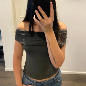 Mörkgrå offshoulder topp - Säljer en stilren mörkgrå offshoulder topp som sitter tight och framhäver axlarna. Perfekt för en trendig look. Passar bra till jeans eller kjol för en avslappnad stil.