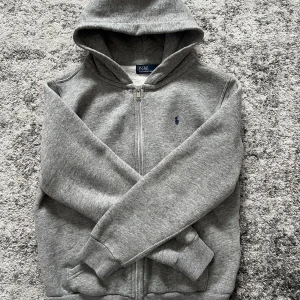 Grå zip hoodie från Polo Ralph Lauren - Säljer grå zip hoodie från Polo Ralph Lauren med dragkedja och huva. Tröjan är i bra skick och materialet är extremt mjukt och mysigt. 