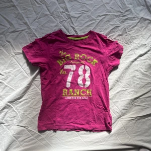 Rosa t-shirt med tryck - Säljer en cool rosa t-shirt med tryck i grönt och vitt. Texten 'The Big Rock Ranch No. 78' 