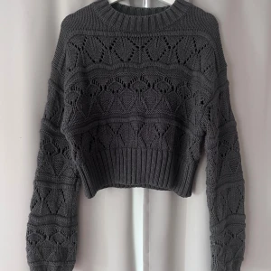 Grå stickad tröja från Gina Tricot - Säljer en snygg grå stickad tröja från Gina Tricot. Tröjan har ett fint stickmönster och är croppad med långa ärmar🖤
