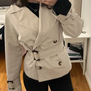 Beige trenchcoat med bälte Nelly - Snygg beige trenchcoat med dubbelknäppning och bälte i midjan. Aldrig använd. Slutsåld på Nellys hemsida. Storlek XXS men skulle säga att den passar som XS. Säljs för 699 på hemsidan.