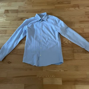 Ljusblå skjorta från Zara - Säljer en stilren ljusblå skjorta från Zara i slim fit. Skjortan har långa ärmar och knappar framtill. Perfekt för en elegant look.