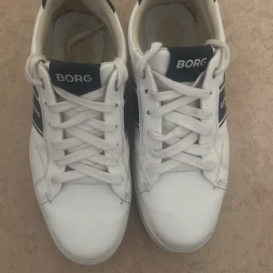 Vita sneakers från Björn Borg - Säljer dom här Snygga vita sneakers från Björn Borg med svarta detaljer jag säljer dem på grund av att dom bara står i garderoben skorna har andvändts en gång men är fortfarande i bra skick och ser ut som nya 