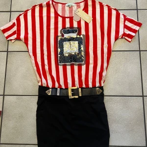 Röd- och vitrandig klänning med paljettdetalj - Säljer en cool röd- och vitrandig klänning. Toppen har korta ärmar och en stor paljettdetalj framtill som föreställer en parfymflaska. Perfekt för att sticka ut i mängden!