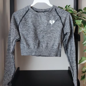 Grå sporttopp från Womens Best i storlek M - Grå melerad sporttopp från märket Women's Best. Storlek M. Väldigt stretchig i materialet. Intakta loggor fram och bak. Känns som ny, knappt blivit använd. Toppen har även tummhål. Resår i nederkant.