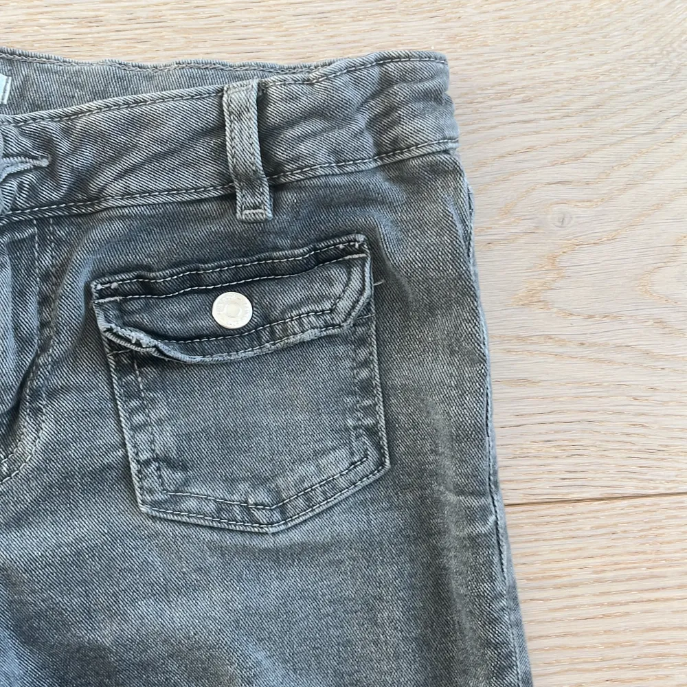 Snygga grå jeansbyxor från Gina Tricot med bootcut-stil. Byxorna har klassiska femficksdetaljer och bälteshällor. Perfekta för en avslappnad look.. Farkut & Housut.
