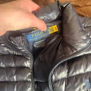 Marinblå dunjacka från Ralph Lauren - Säljer en snygg mörkblå dunjacka från Ralph Lauren. Jackan har aningen glansig yta, men betydligt mattare i verkligheten. Perfekt för våren med sin stilrena design och bekväma passform. Gott skick med ett nypris på 4000kr, Kom med prisförslag! Självklart är jackan äkta! Tar även emot byten!