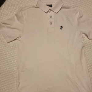 Vit pikétröja från Peak Performance - Vit pikétröja från Peak Performance. Tröjan har en klassisk krage med tre knappar och en diskret logga på bröstet.