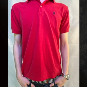 Röd pikétröja från Ralph Lauren - Säljer en klassisk röd pikétröja från Ralph Lauren med korta ärmar och en liten broderad logga på bröstet. Perfekt för en stilren och avslappnad look. Tröjan har en krage med två knappar. Storlek L men passar mer M. Skriv till oss för att diskutera pris