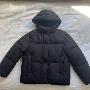 Svart pufferjacka från Zara - Säljer en svart pufferjacka från Zara i storlek 164. Jackan har en mysig huva och långa ärmar, perfekt för kyliga dagar. Den är quiltad för extra värme och stil. Passar både till vardags och när du vill hålla dig varm och bekväm.