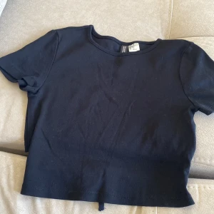 Svart croppad topp med knyt - Säljer en svart croppad topp från H&M med korta ärmar och knytning i midjan. Perfekt för en avslappnad stil.