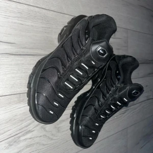 Nike air TN - Inga tecken på användning, säljs pga att de är för små för mig. Säljer ett par svarta Nike sneakers med en sportig design och synlig Air-dämpning i sulan. Skorna har en stilren look med svarta detaljer och en robust yttersula för bra grepp. Perfekta för både vardag och träning.