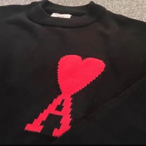 Ami Paris tröja  - Snygg svart tröja från Ami med ett stort rött hjärta och bokstaven A på bröstet. Tröjan har en rund halsringning och långa ärmar. Perfekt för en stilren look.