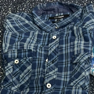 Blå rutig skjorta från KappAhl - Snygg blå rutig skjorta från KappAhl i slim fit. Skjortan har knappar framtill och två bröstfickor med lock. Perfekt för en stilren look.