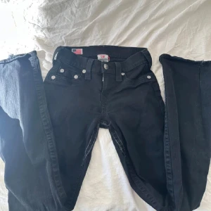 Svarta jeans från True Religion - Svarta bootcut jeans ifrån True Religion! Säljer då de inte passar mig. Midjemåttet rakt över är ca 33cm men de är rätt stretchiga💗 Skriv privat för mer info/bilder💗Jeansen är lågmidjade