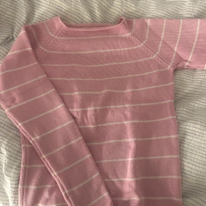 Rosa randig tröja - Säljer en söt rosa tröja med vita ränder. Tröjan har långa ärmar och en klassisk rund hals. Perfekt för en avslappnad stil. Passar bra till jeans eller kjol.