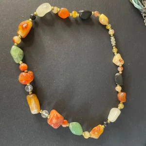 Färgglatt halsband med stenar - Unikt halsband med stora, färgglada stenar i grönt, orange, svart och beige. Perfekt för att ge en bohemisk touch till din stil. Stenarna är ojämna och ger ett naturligt utseende.