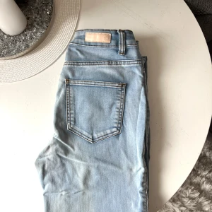 Ljusblå jeansbyxor - Säljer ett par ljusblå jeansbyxor med klassisk femficksdesign och knappgylf. Byxorna har en normal passform och är perfekta för en avslappnad stil. De är tillverkade i ett mjukt och bekvämt denimtyg.