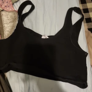 Svart linnetopp från H&M - Säljer en stilren svart linnetopp från H&M:s Basic-kollektion. Toppen har breda axelband och en enkel design som passar perfekt till vardags. Perfekt för lager-på-lager eller att bära som den är.