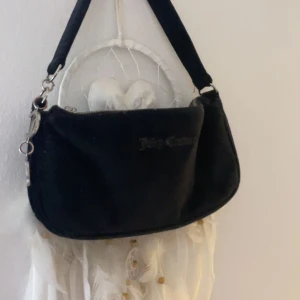 axelväska från Juicy Couture - Snygg svart axelväska från Juicy Couture med silverfärgade detaljer och dragkedja💞Väskan har en  design med märkets logotyp på framsidan och en praktisk axelrem. På dragkedjan så finns det ett J som väldigt änkelt trillar av men kan säkerts lagga på något sätt, den är lite rostig på bokstäverna men annars inga skador💞Kan diskutera pris
