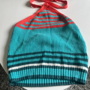 Randig stickad halterneck-topp - Säljer en färgglad stickad halterneck-topp med ränder i turkos, röd och vit. Toppen har en knytning i nacken 