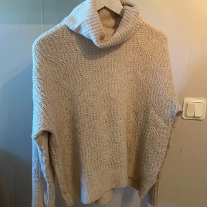 Beige stickad polotröja från 157 - Mysig beige stickad polotröja från 157 med kabelstickat mönster. Tröjan har en hög polokrage och långa ärmar, perfekt för kyliga dagar. Enkel att matcha med olika outfits och superbekväm att bära.