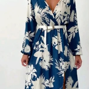 Blåvit långklänning med blommigt mönster och bälte - Snygg långklänning i blått och vitt med blommigt mönster. Klänningen har omlottmodell, v-ringning, lång ärm och ett vitt bälte i midjan. Perfekt för sommarens alla tillfällen.