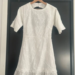 Vit blommig klänning från NA-KD - Superfin vit klänning från NA-KD med broderade blommor och volangdetalj nertill. Passar perfekt till studentklänning!