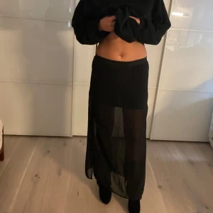 Svart långkjol i transparent material - Säljer en svart långkjol med transparent tyg. Kjolen har en rak passform och är perfekt för dig som vill ha en stilren men ändå cool outfit. Passar till många olika tillfällen och är lätt att matcha med olika toppar.