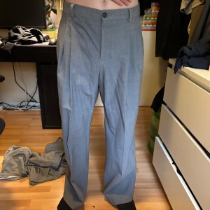 Ljusgrå kostymbyxor med pressveck - Snygga ljusgrå kostymbyxor med klassiskt rakt snitt och pressveck framtill. Byxorna har hällor för bälte, dold dragkedja och knapp i midjan. Perfekta för en dressad look.