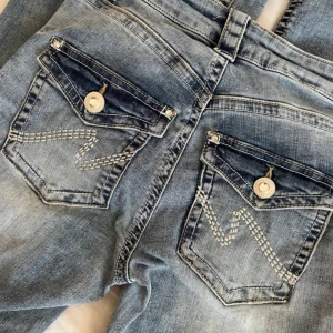 Blå jeansbyxor från Nelly med dekorativa bakfickor - Snygga blå jeansbyxor från Nelly med ljus tvätt och dekorativa sömmar på bakfickorna. Byxorna har normal passform, klassisk femficksdesign och knappgylf. Perfekta för en avslappnad stil. Köpt för 799kr och är helt nya med prislapp kvar.